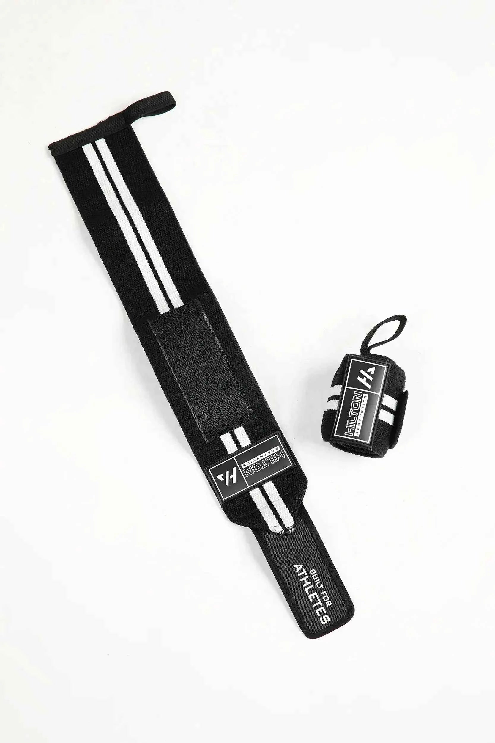 Black Hilton Aesthetics weightlifting wrist wraps with thumb loops, flat-lay view